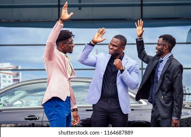 A Group Of Their Three Successful African American Businessmen In A Stylish Suit Talking And Rejoicing On The Street Skyscraper Window Background. Teamwork And Success Concept