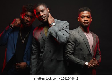 Group Of Three African Friends Dressed In Stylish Suits Posing Isolated In Studio Over Dark Background. Classmates Have Grown Up And Become Successful People. People, Fashion Condept