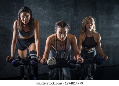 Group of three attractive sporty girls working out on exercise bicycles during cycling class indoors.