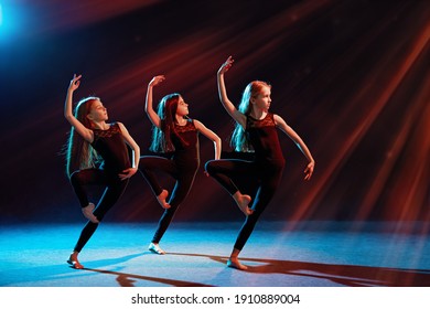 group of three ballet girls in tight-fitting costumes dance against a black background with their long hair down, silhouettes illuminated by color sources.