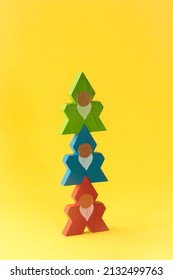 A group of three brightly colored, old-fashioned stacking wooden toy cut-out troll or elf figurines stacked on top of one another on a yellow background. Concept of play, teamwork and cooperation.
