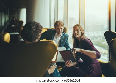 Group Of Three Business People Having Work Meeting On High Floor Of Skyscraper In Luxury Office Interior: Caucasian Handsome Boss Looking At Screen Of Digital Tablet Shown By His Female Colleague