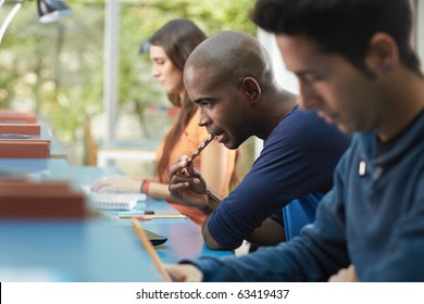 Group Of Three College Students Studying In Library, One Of Them Eating A Snack. Horizontal Shape, Side View, Waist Up, Copy Space