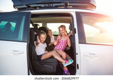 Group of three cute adorable little happy caucasian children enjoy having fun sit in minivan going to sea beach road trip on hot summer day. Kids in swimsuit in car with side open door against sun