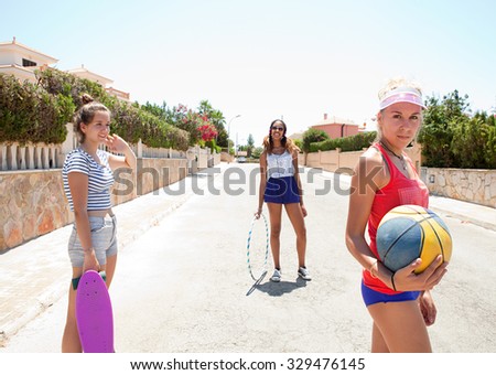 Group of three diverse adolescent girls enjoying time together in a suburban area, playing with skateboard, and basketball on a weekend vacation, outdoors. Teenager technology lifestyle, exterior.