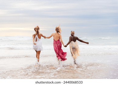 group of three female friends of different races (Latina, white and black) enjoy a day at the beach running together and holding hands along the seashore on a beach. - Powered by Shutterstock