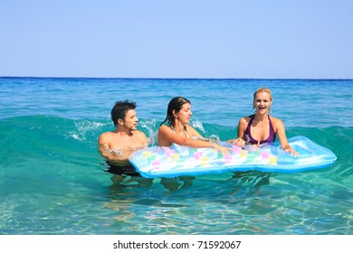 Group Of Three Friends - Man And Women - On The Beach Having Lots Of Fun In Their Vacation In Greece