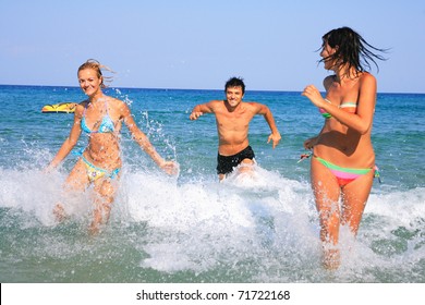 Group Of Three Friends - Man And Women - On The Beach Having Lots Of Fun In Their Vacation In Greece