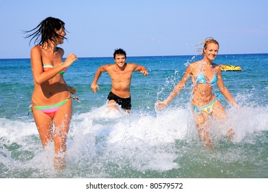 Group Of Three Friends - Man And Women - On The Beach Having Lots Of Fun In Their Vacation In Greece