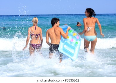 Group Of Three Friends - Man And Women - On The Beach Having Lots Of Fun In Their Vacation In Greece