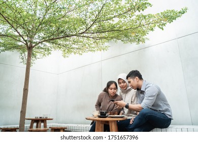 Group Of Three Friends Using Smartphone Hang Out In Cafe