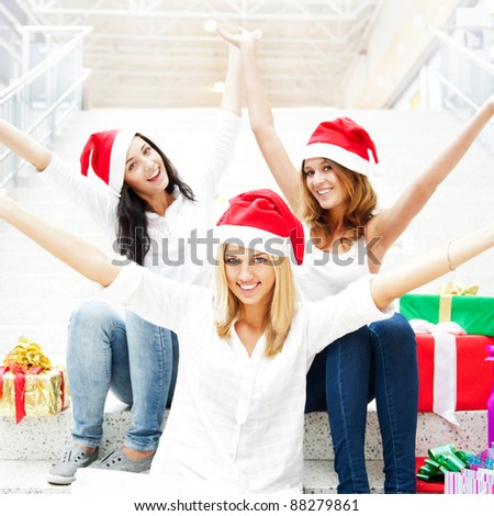 Group of three happy pretty girls are celebrating christmas and new year holidays wearing santa clause red hats and laughing with open arms