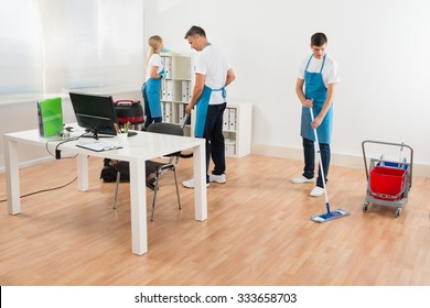 Group Of Three Janitors Together Cleaning Modern Office