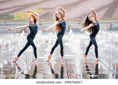 a group of three little ballerinas in black tight-fitting suits dance against the backdrop of city fountains on a hot day. - Powered by Shutterstock