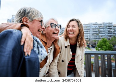 Group of three mature caucasian women enjoying embracing walk together laughing outdoor. Senior female friends having fun hugging strolling happy in the urban city street. Elderly people enjoying - Powered by Shutterstock