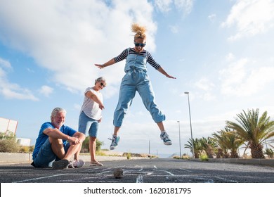 Group Of Three People Of Different Ages Playing Together At The Hopscotch - Mature Man Sitting On The Ground - School Game And Having Fun