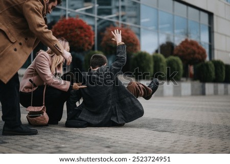 A group of three professionals helping their colleague who has stumbled and fallen on the pavement outside a modern office building.