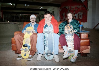 Group of three self-confident gen Z Caucasian skateboard riders in streetwear sitting on couch posing for camera, flash photo - Powered by Shutterstock