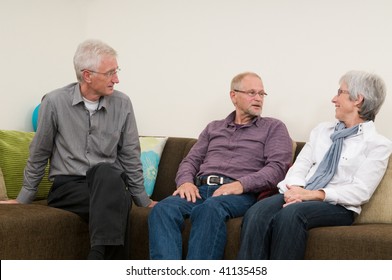 Group Of Three Seniors Talking And Laughing On A Couch At Home.