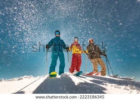 Group of three skiers stands against sun and snowfall. Ski resort concept