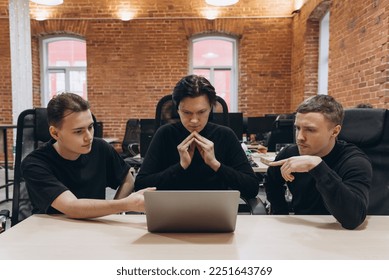 group of three software developers young men in black clothes working with notebook in vintage office with red brick walls, discussion about work