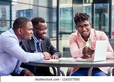 A group of three stylish African American students entrepreneurs in fashion business suits working sitting at table with laptop in a summer cafe outdoors - Shutterstock ID 1161077050