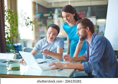 Group of three successful business partners in casual discussing data in laptop at meeting in office