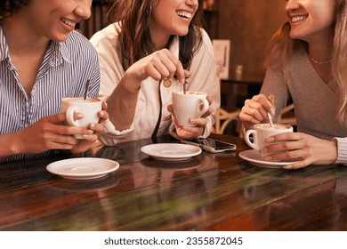 Group of three unrecognizable girl friends drinking coffee sitting in a table of a cafe. They show their friendship while they have fun. We only see their smiles not the rest of the faces. - Powered by Shutterstock