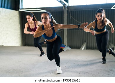 Group of three women doing lateral bounds together in a high-intensity interval class at the gym. Beautiful women in sportswear exercising with a cardio workout