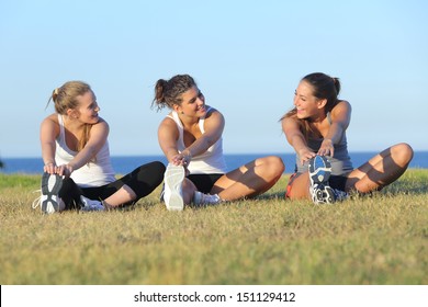 Group of three women stretching after sport on the grass with the sea in the background            