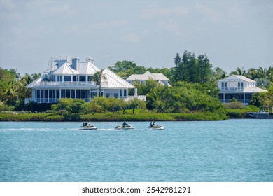 A group of three women and two men ride three water scooters together past a large seaside house on a barrier island along the Gulf Coast in southwest Florida. Light digital oil-painting effect. - Powered by Shutterstock