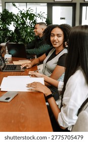 A group of three workers are sitting at a table while two of them are talking and two of them are smiling
