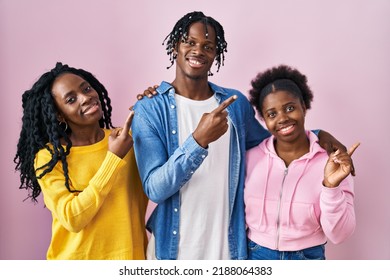 Group Of Three Young Black People Standing Together Over Pink Background With A Big Smile On Face, Pointing With Hand Finger To The Side Looking At The Camera. 