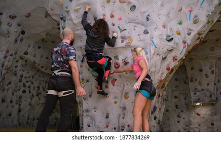 Group Of Three Young Friends Wearing Protective Face Masks Climbing A Wall On Artificial Rock Climbing Wall Indoors. Extreme Sports In The New Normal.