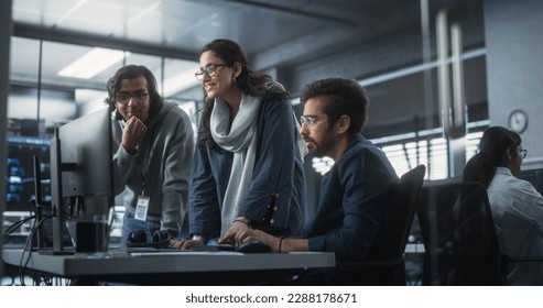 Group of Three Young Indian Software Engineers Use Computer to Discuss a Technological Project in Modern Industrial Office. Group of Male and Female Scientists Work in Research and Development Center - Powered by Shutterstock