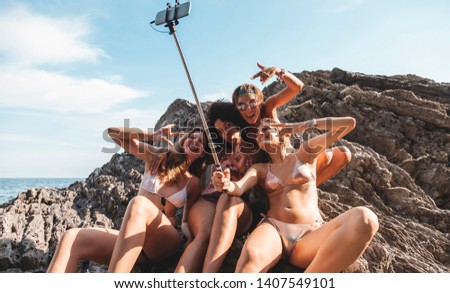 group of three young multiracial female friends taking a selfie on a rock in the middle of the sea. summer vacation concept