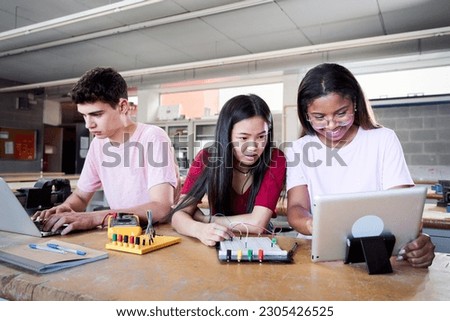 Group of three young students from a technical high school doing a technological team project. People using the computer consulting doubts about their practices in electronic technology class.