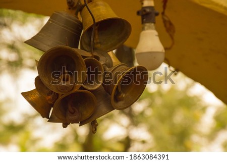 Group of tiny bronze bells hanging on a ceiling of a ancient Hindu temple. Light emitting diode bulb in the blurred background. Picture captured at old Hindu temple Kolhapur, Maharashtra, India.