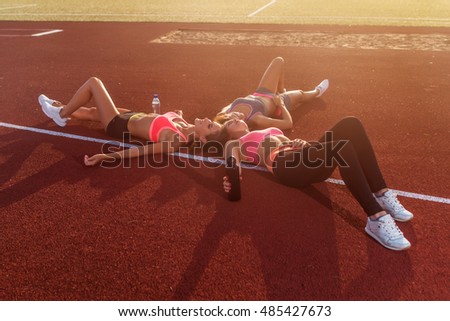 Group of tired fit girls lying on stadiun in circle outdoors