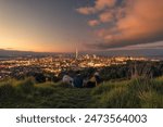 Group of tourist relaxing on Mount Eden with cityscape iconic sky tower during the sunset in central of Auckland at New Zealand