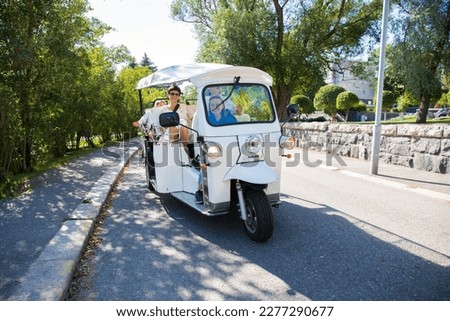 A group of tourists driving through the city center in tuk-tuk electric car. Travelers enjoying a ride on environmentally friendly transport in the old town