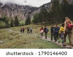 Group of tourists hike to Rothbach waterfall throw pine forest on background of rock mountains & cloud sky. Bavaria. Germany
