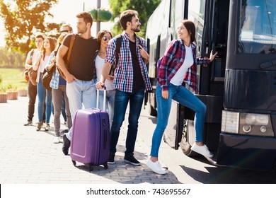 A group of tourists preparing to get on the bus. The guy with the girl goes into the bus and brings in their luggage. The girl goes first. Behind them is a group of tourists who are waiting.