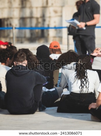 Group of tourists sitting during outdoor excursion tour in the city streets with guide, a docent with a tourist adult visitors, school college field trip, students urban tour in a summer sunny day
