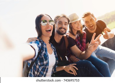 A group of tourists are sitting in a park on a bench. A girl in glasses makes selfie with her friends. They are posing and smiling. Each of them has a backpack for traveling. - Powered by Shutterstock