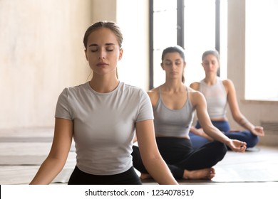 Group training of deep meditation at yoga studio class. Diverse young females sitting with closed eyes in lotus position meditate and visualizing together, feeling self-awareness serenity and calmness - Powered by Shutterstock