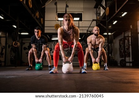 Group training in a modern and fully equipped gym. Three friends lift heavy weights, do squats and sweat in their sportswear. Healthy lifestyle.