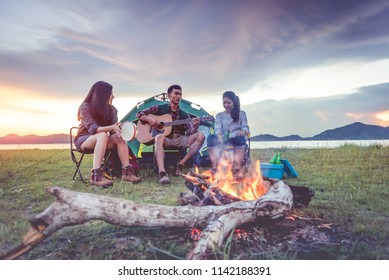 Group of travelers camping and doing picnic and playing music together. Mountain and lake background. People and lifestyle. Outdoors activity and leisure theme. Backpacker and Hiker. Dawn and twilight - Powered by Shutterstock