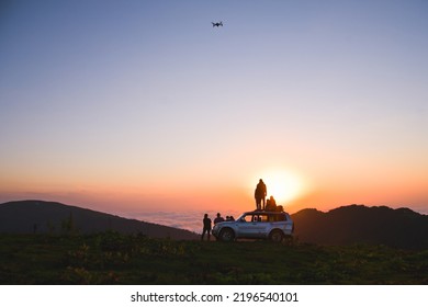Group Of Travelers Content Creators Stand By On 4wd Vehicle Together And Fly Drone Film Inspirational Landscape For Socials. Shoot Selfie Watch Sunset; Capture Travel Moments.Exploration And Adventure