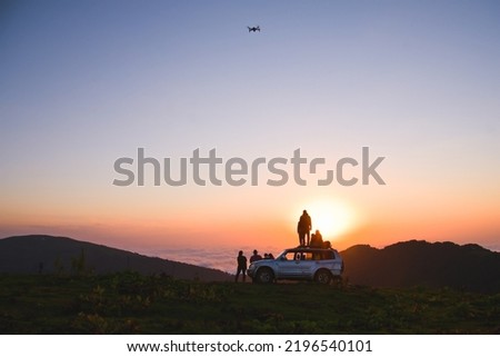 Group of travelers content creators stand by on 4wd vehicle together and fly drone film inspirational landscape for socials. Shoot selfie watch sunset; capture travel moments.Exploration and adventure